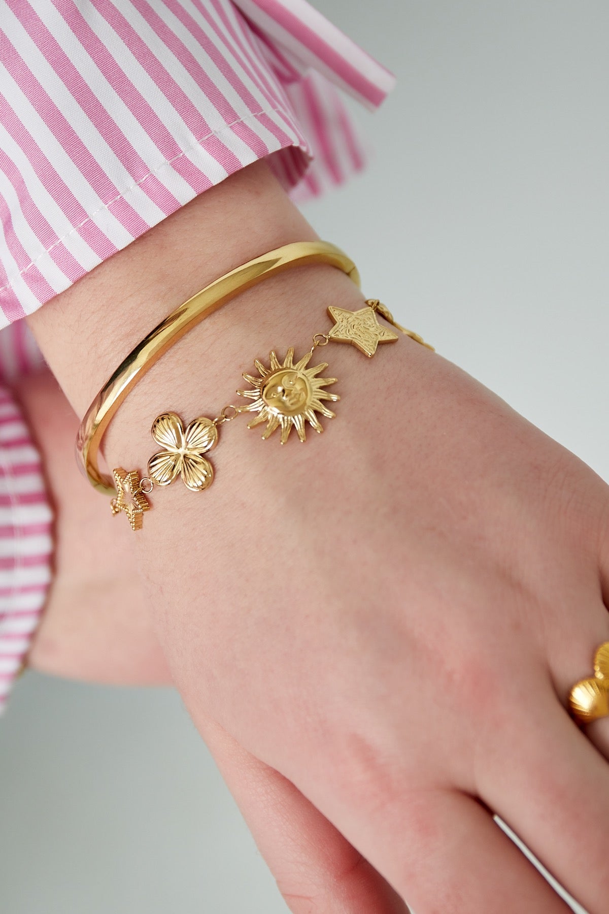Statement schakelarmband met figuurtjes van een ster, een bloem, een zon, en een strik goud